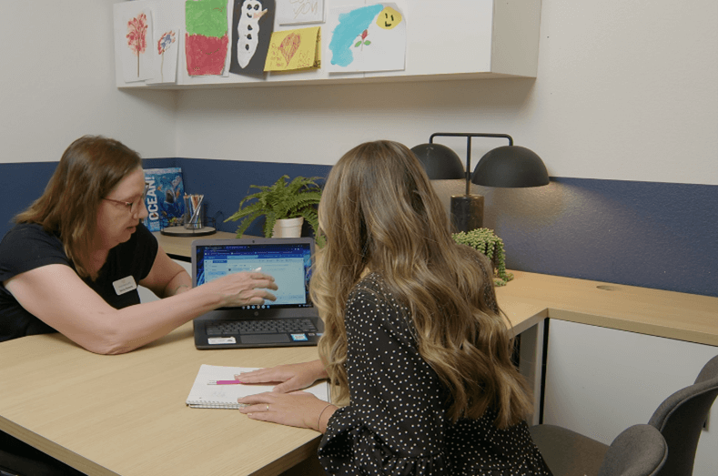 Two women sitting at a desk looking over a laptop