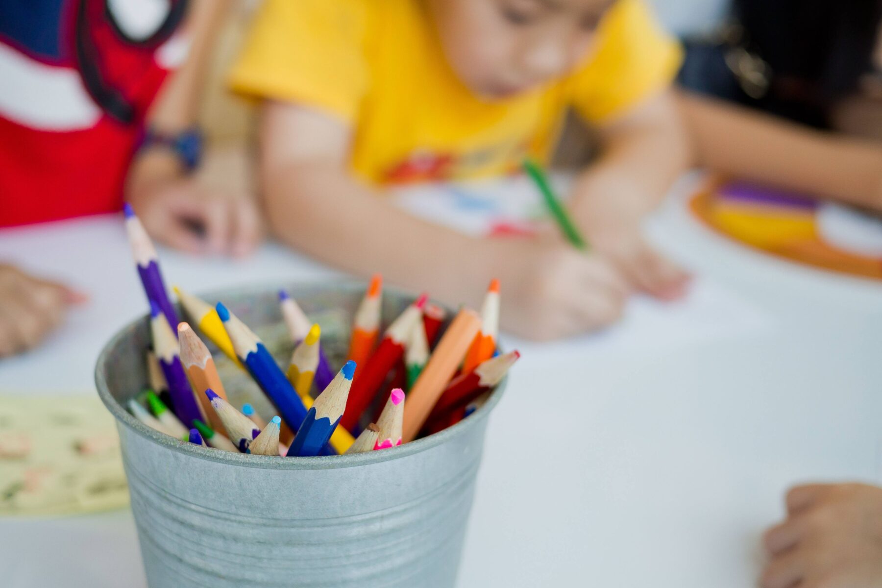 Kids coloring at a table with a bucket of colored pencils in the middle